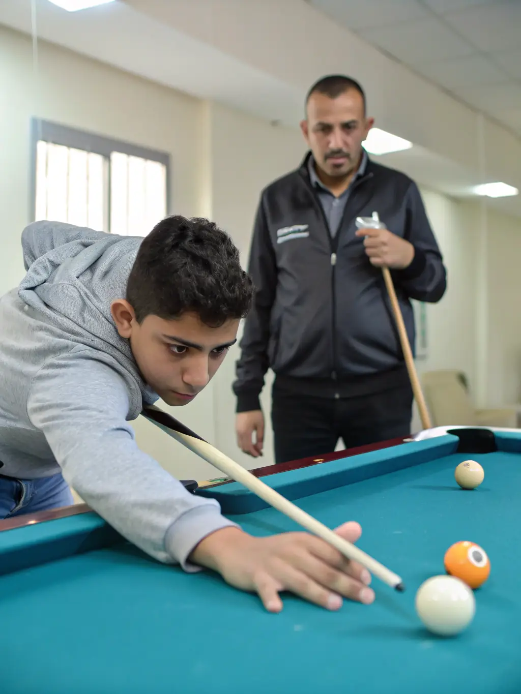 A focused shot of a youth billiards training program, highlighting young players learning the fundamentals of the game with guidance from instructors.